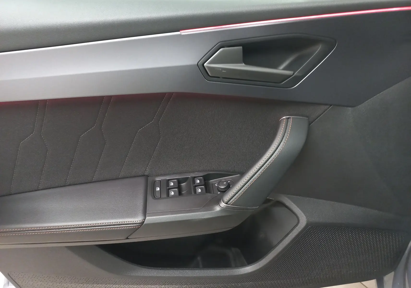 Vue rapprochée de la porte intérieure côté gauche de la CUPRA Leon Phase 2, avec garniture noire et surpiqûres orange.