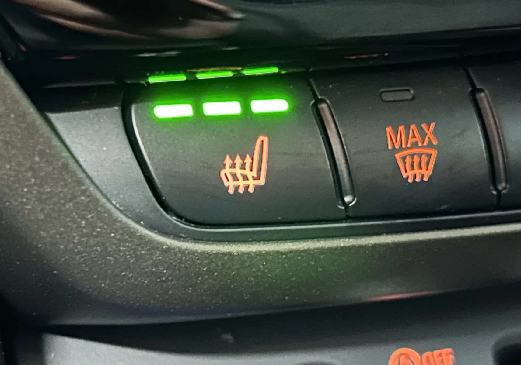 Gros plan sur les boutons de commande du siège chauffant et du dégivrage avant dans une MINI Countryman vert métallique.