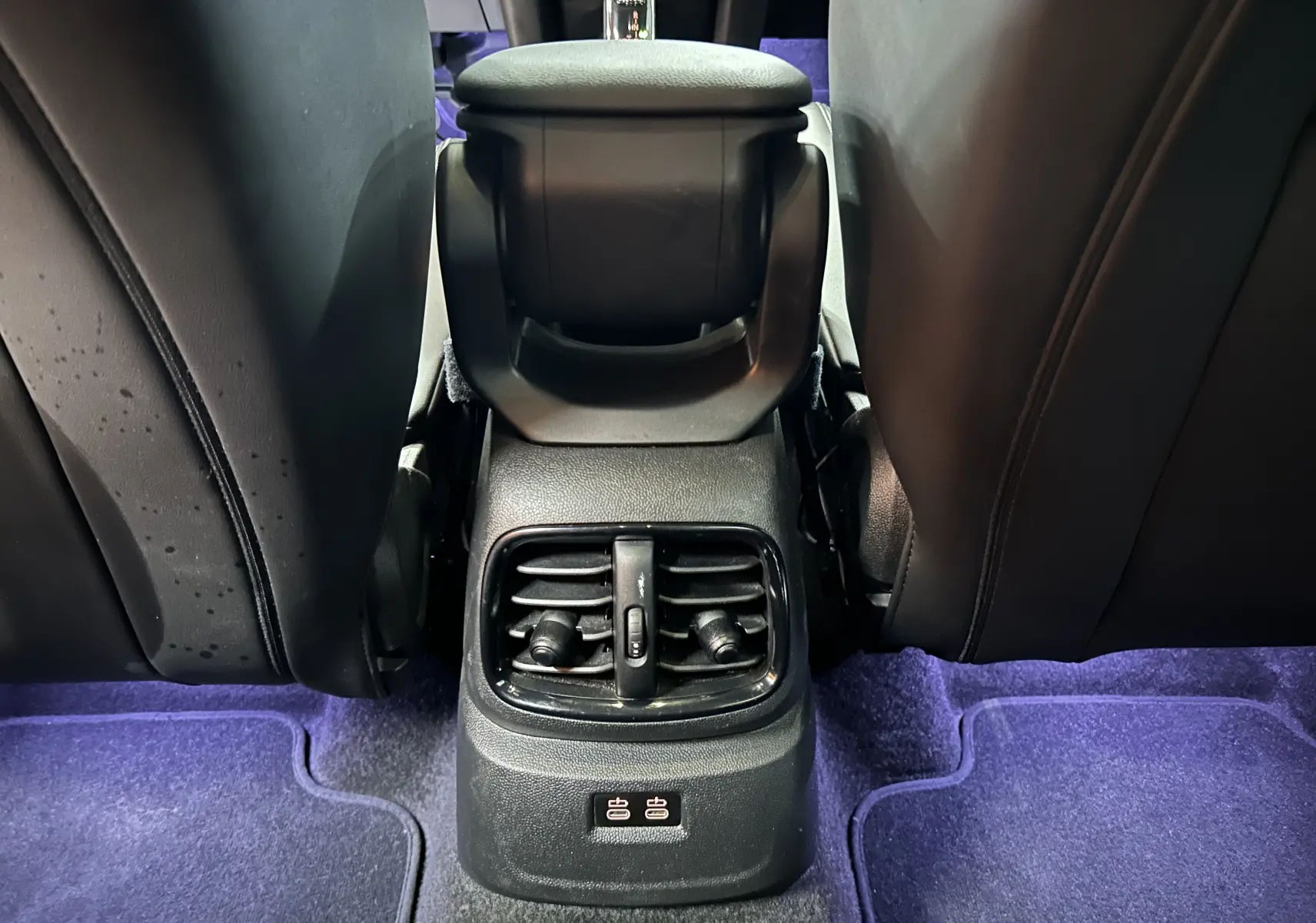 Vue rapprochée de la console arrière avec aérateurs et ports USB, sièges en cuir noir, tapis violet dans MINI Countryman 2021.