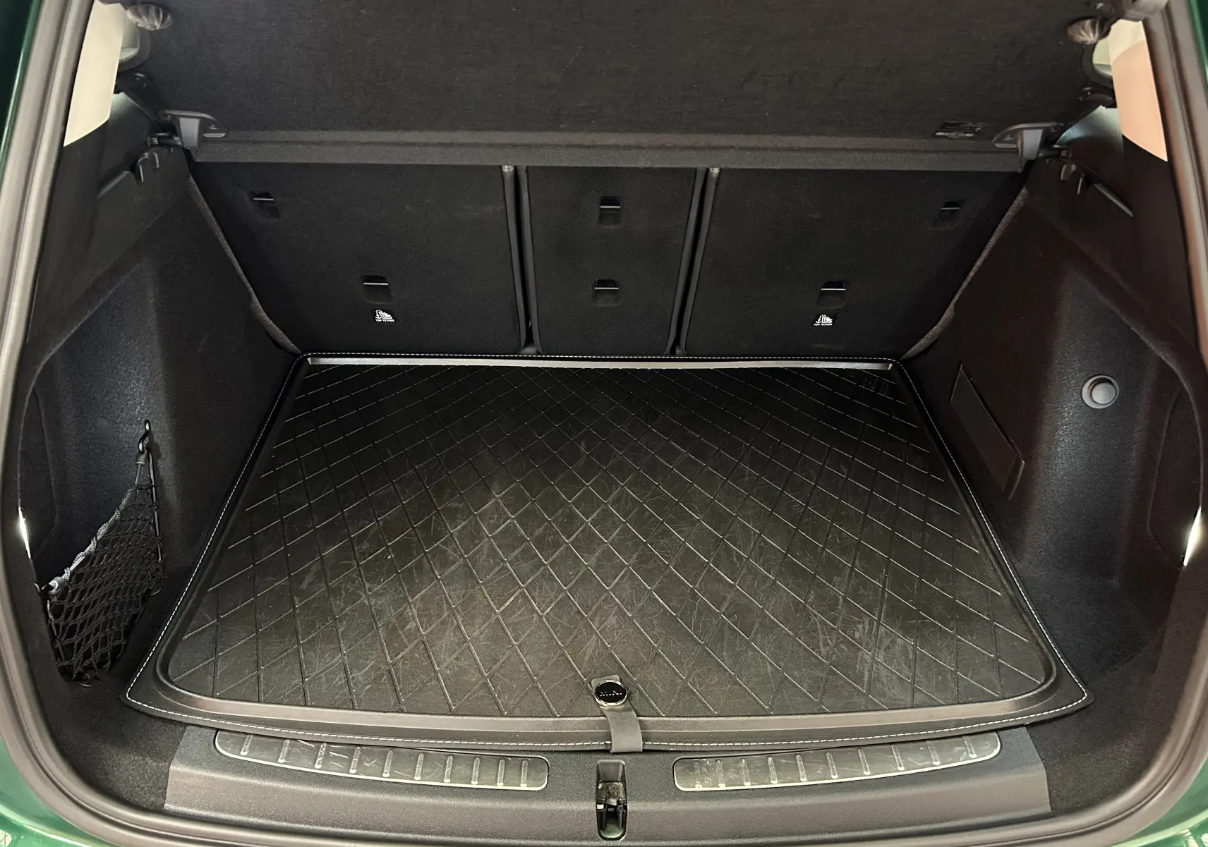 Coffre ouvert vu de l'arrière d'une MINI Countryman vert métallisé avec tapis de protection noir matelassé.