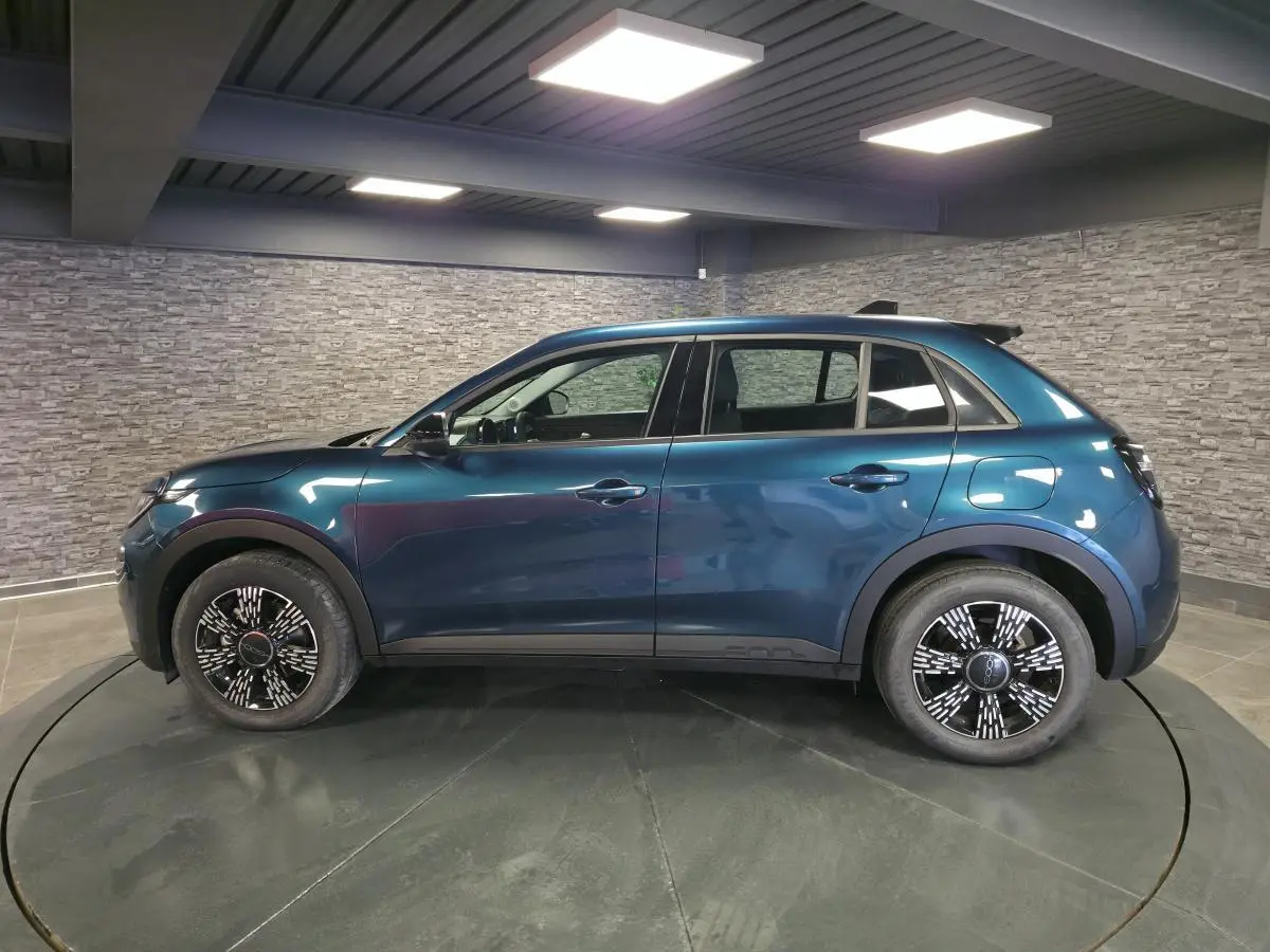 Vue de profil côté gauche d'un FIAT 600 1.2 Hybrid bleu métallisé avec jantes alliage et toit noir en intérieur showroom.
