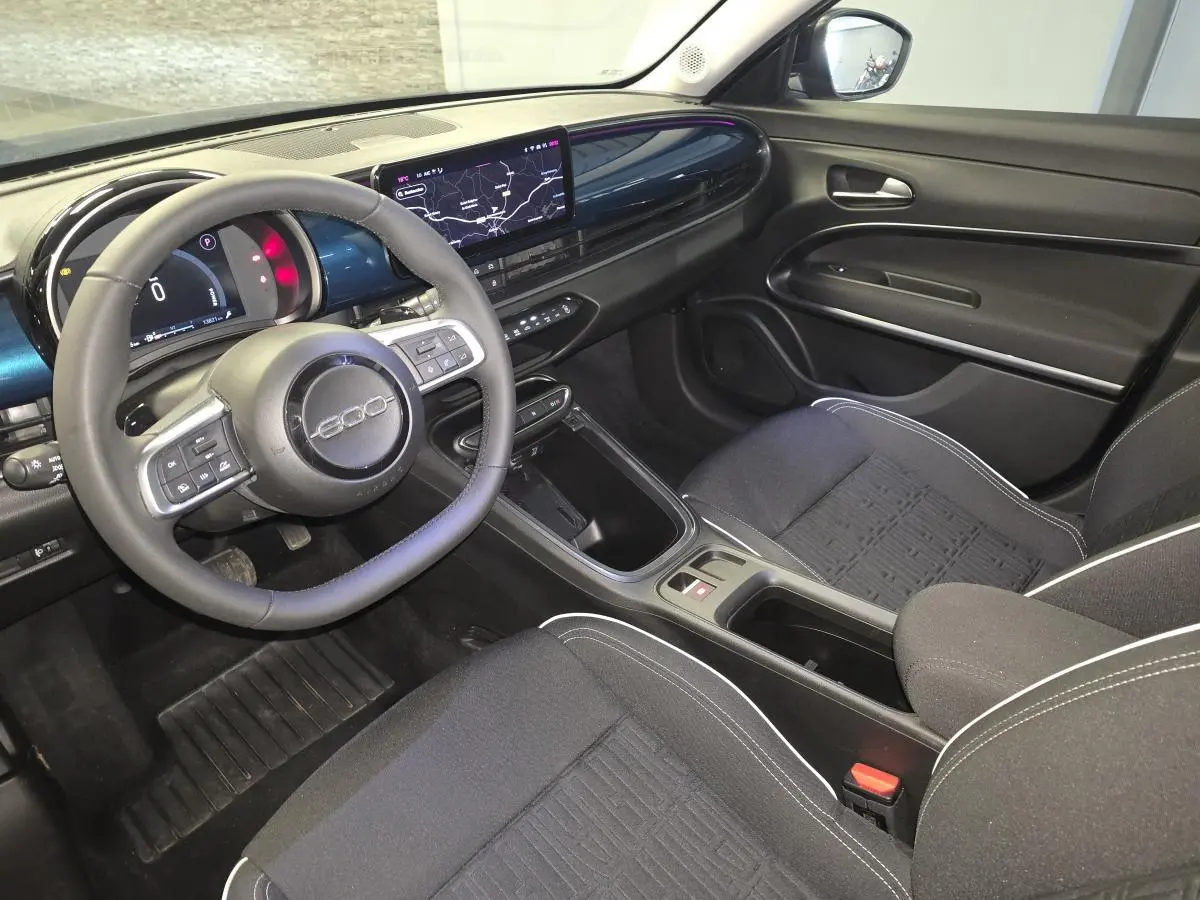 Vue intérieure côté conducteur de la FIAT 600 Hybrid 2025 avec tableau de bord bleu et volant multifonction noir.