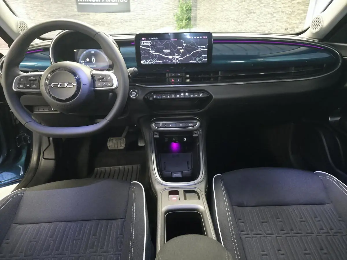 Vue intérieure avant de la Fiat 600 hybride bleue, tableau de bord avec écran central tactile et éclairage d'ambiance violet.