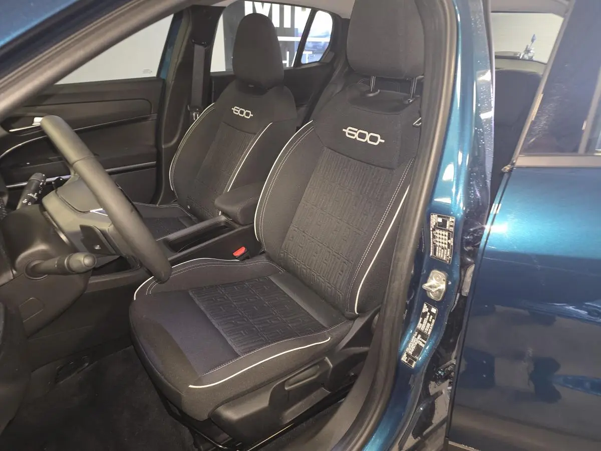 Vue intérieure côté conducteur de la FIAT 600 Hybrid 2025 bleu, sièges noirs avec logo "600" brodé et surpiqûres blanches.