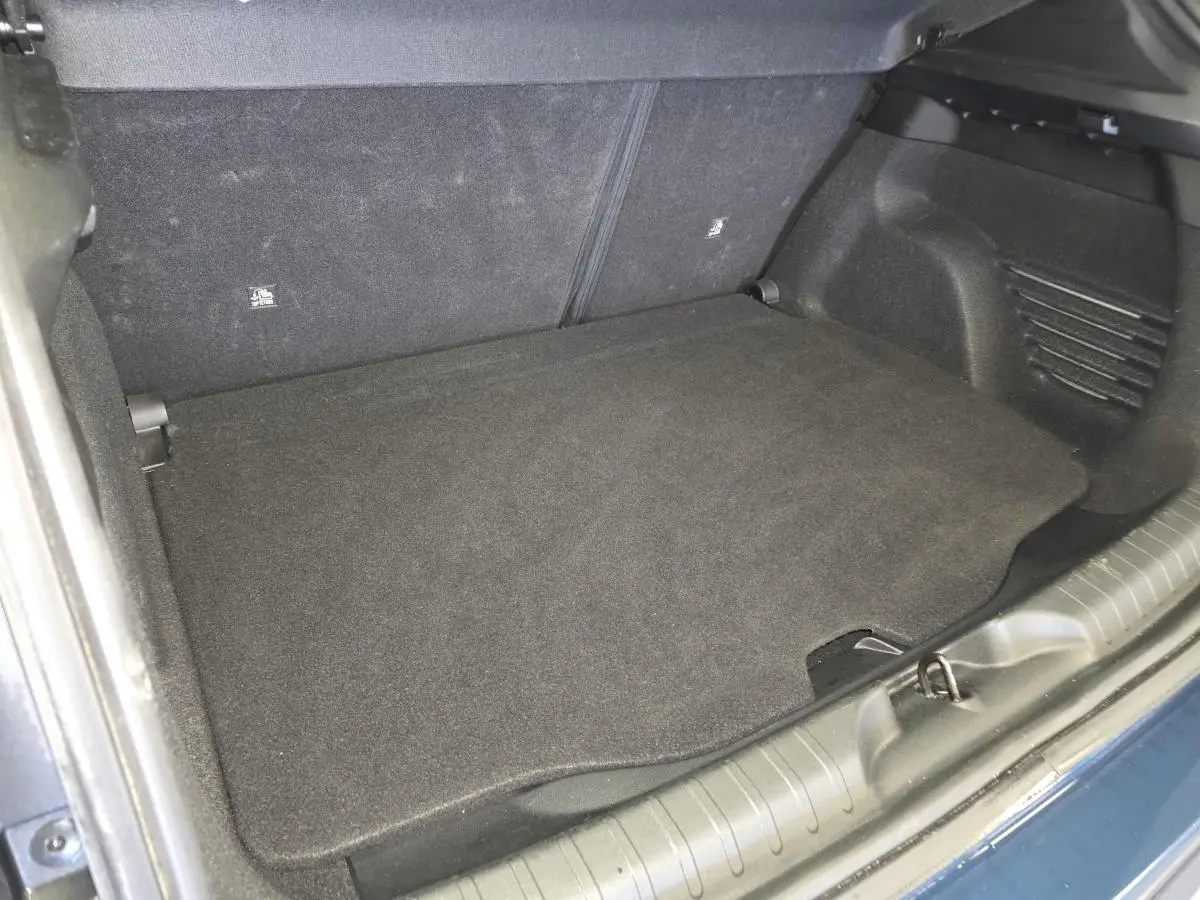 Coffre ouvert vu de dessus d'une FIAT 600 bleu, montrant le plancher de coffre noir et les sièges arrière rabattus.