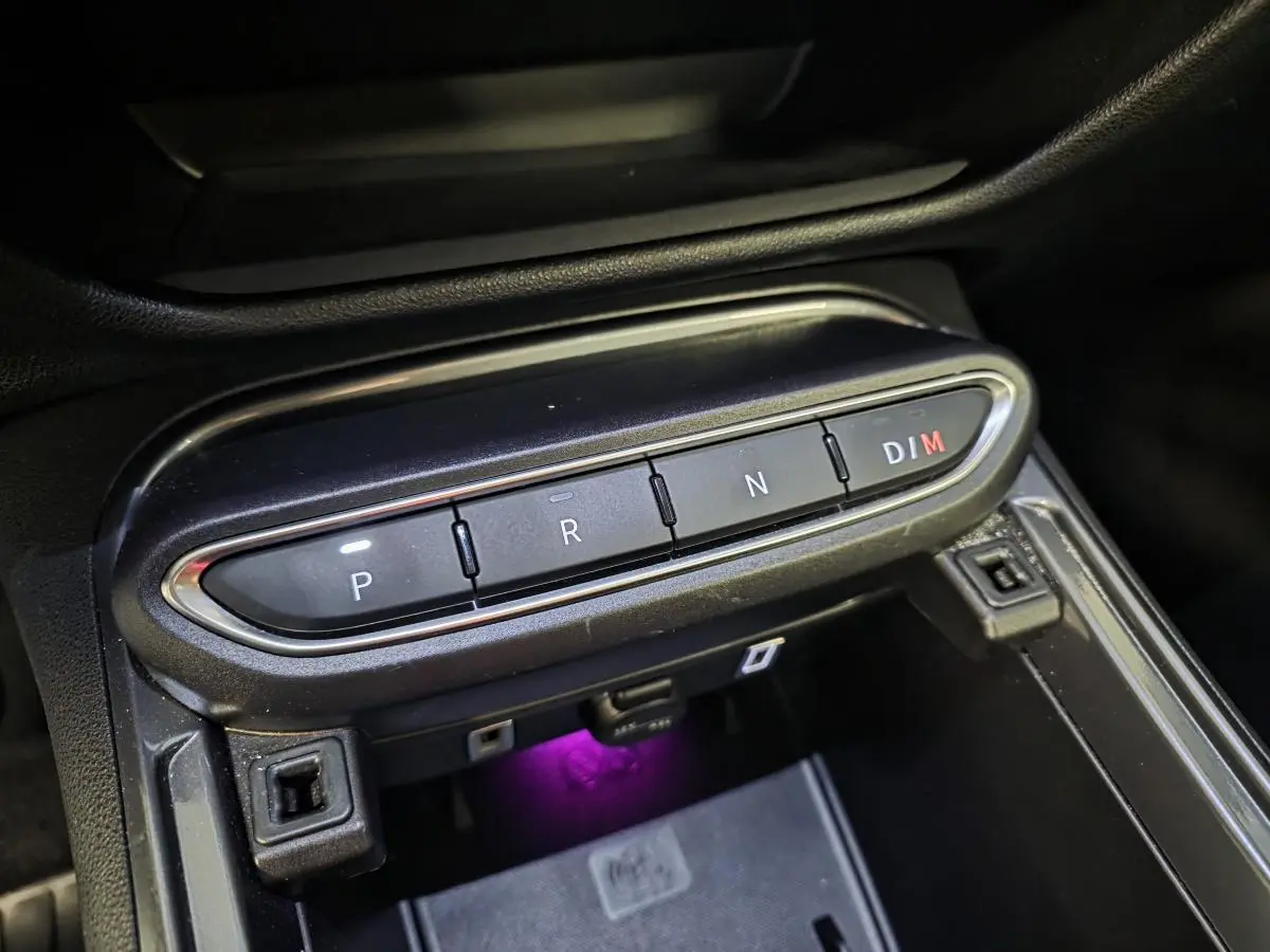 Gros plan sur la console centrale noire avec boutons de boîte auto et éclairage violet sous la prise USB, Fiat 600 Hybrid 2025.