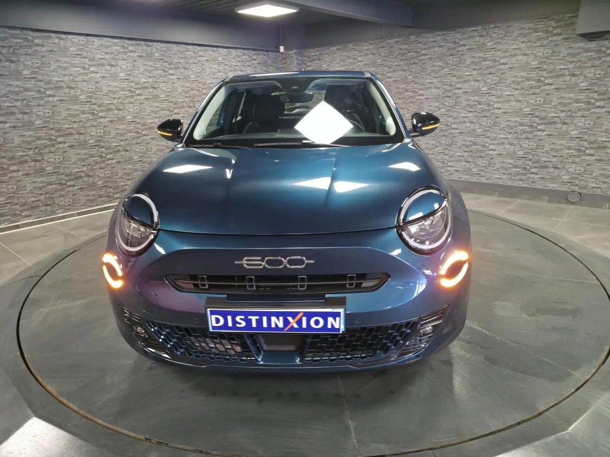 Vue frontale d'une FIAT 600 hybride bleu métallisé avec feux de jour LED allumés en intérieur showroom.
