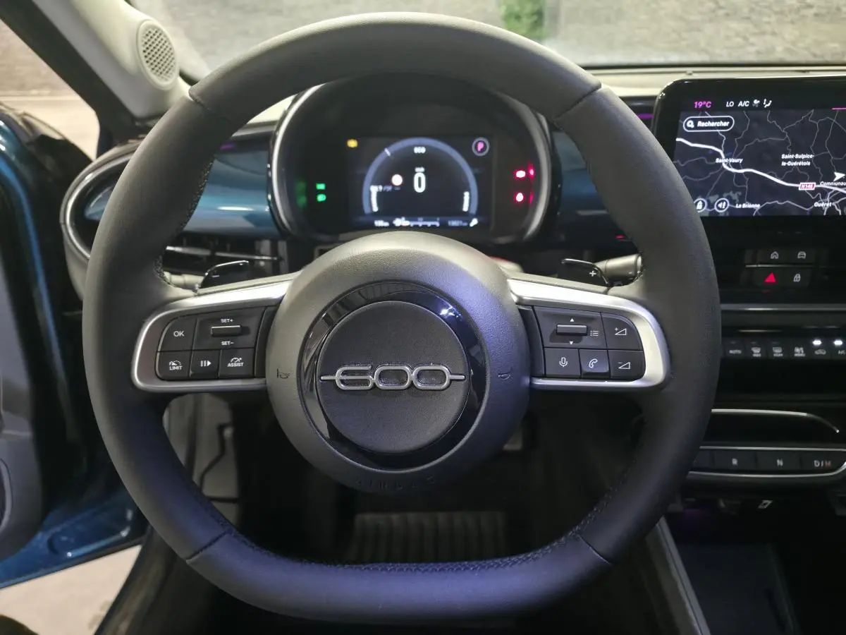 Vue intérieure centrée sur le volant noir de la Fiat 600 1.2 Hybrid 2025 avec tableau de bord numérique et écran tactile.