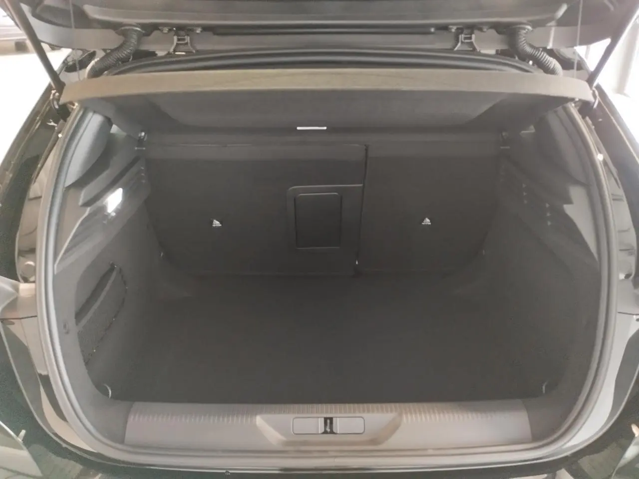 Coffre ouvert vu de l'arrière d'une Peugeot 308 noire métallisée, montrant un espace de rangement vide et propre.