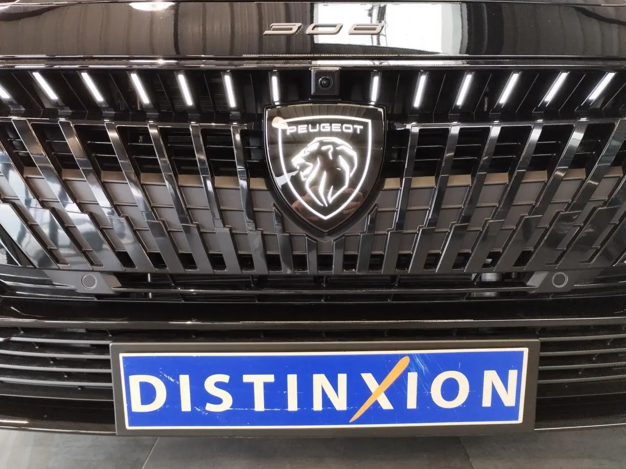 Gros plan sur la calandre noire métallisée de la Peugeot 308 avec logo lion lumineux et plaque Distinxion.