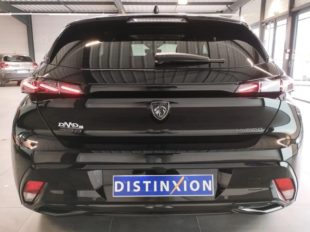 Vue arrière d'une Peugeot 308 hybride noire métallisée avec feux arrière LED en forme de griffes et logo central.