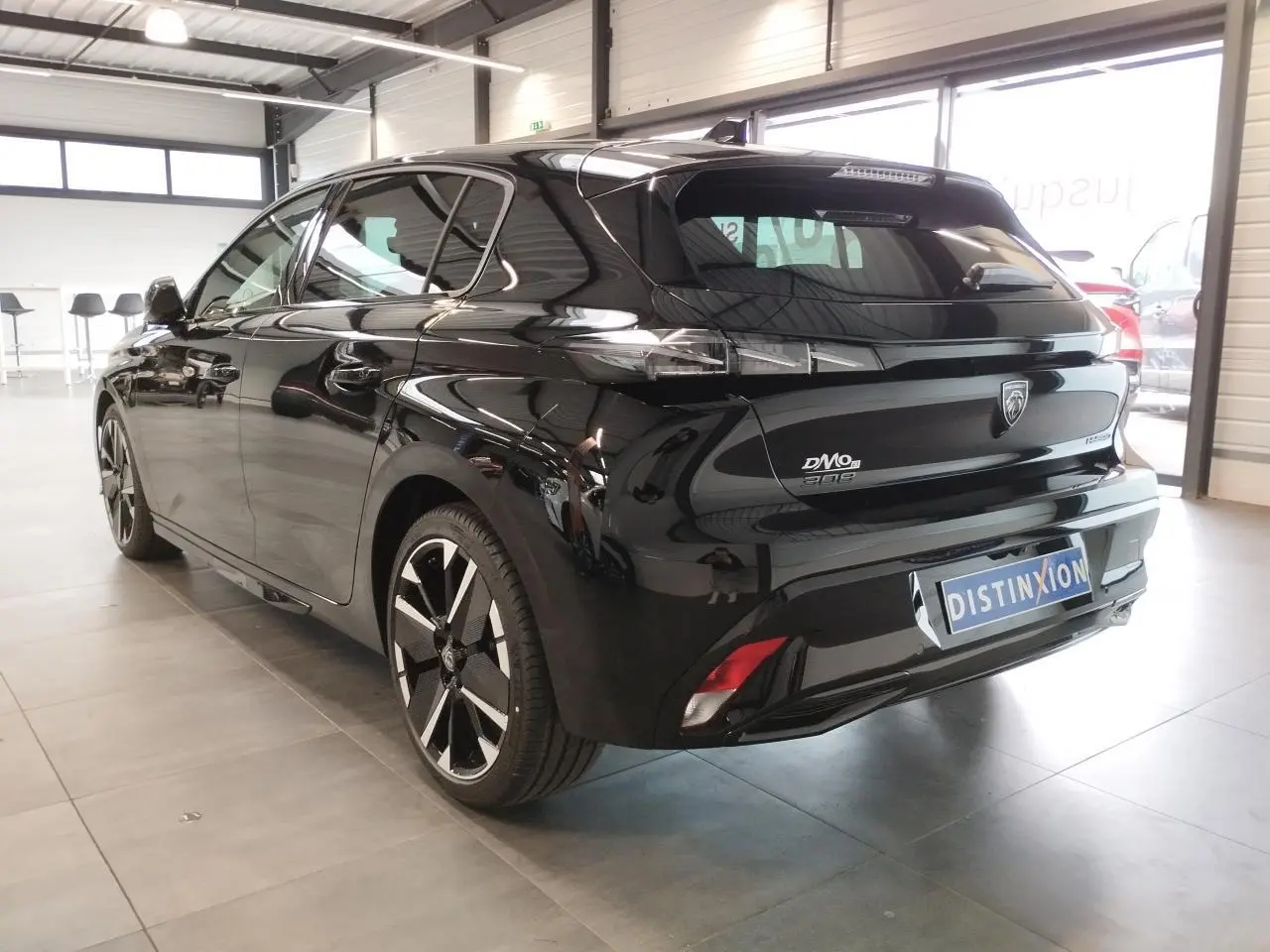 Peugeot 308 hybride noir métallisé vue 3/4 arrière droit en intérieur avec jantes bi-tons et feux LED griffés.