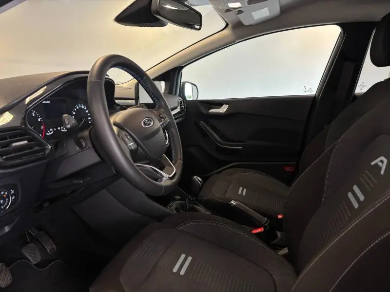 Intérieur avant droit de la Ford Fiesta 2022 avec sièges noirs et tableau de bord moderne au volant multifonction.
