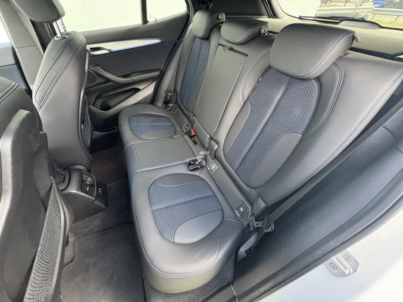 Vue intérieure arrière du BMW X2 blanc alpin, sièges arrière en tissu et similicuir noir avec inserts bleus.