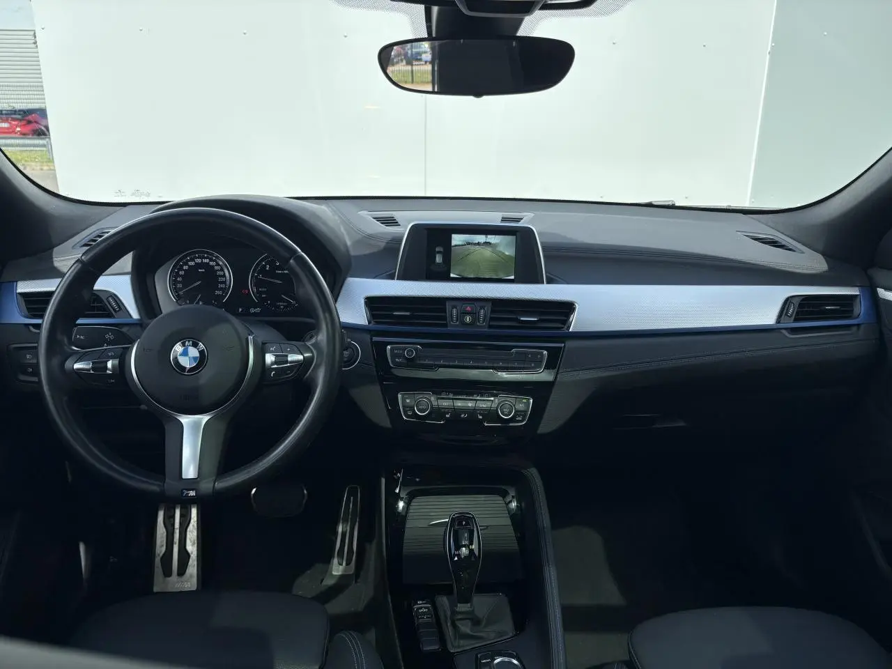 Intérieur BMW X2 vue de face, tableau de bord noir avec écran central et volant M Sport cuir.