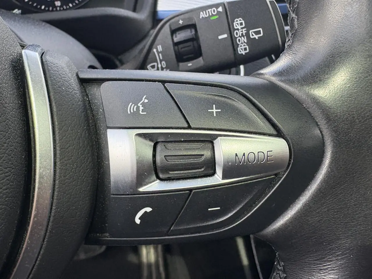 Gros plan sur les commandes multifonctions du volant cuir noir du BMW X2 blanc Alpin, avec bouton mode et volume.