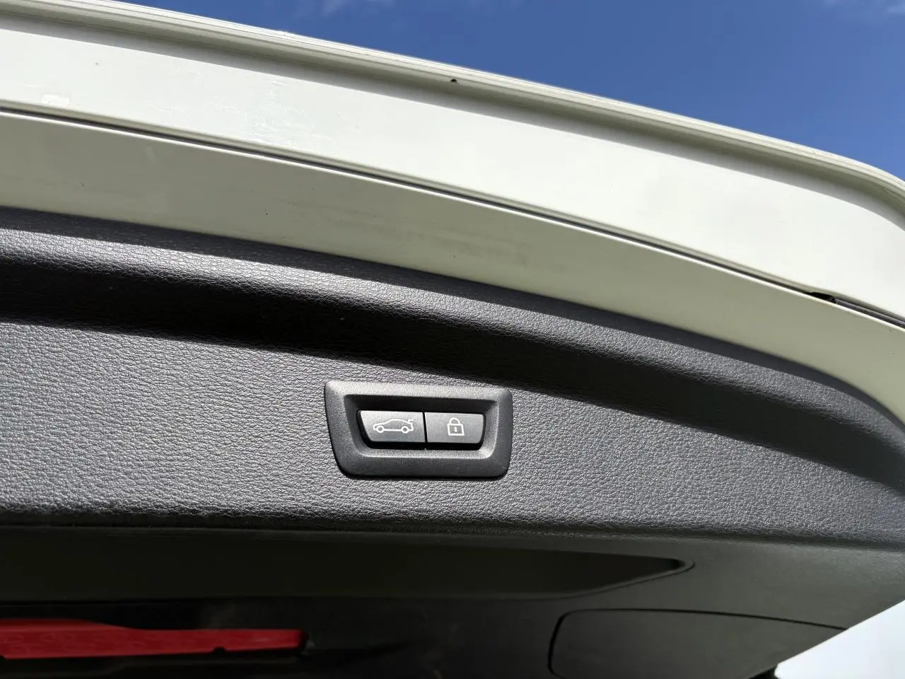 Bouton de commande électrique du hayon sur la partie intérieure du coffre d'un BMW X2 blanc alpin, ciel bleu en arrière-plan