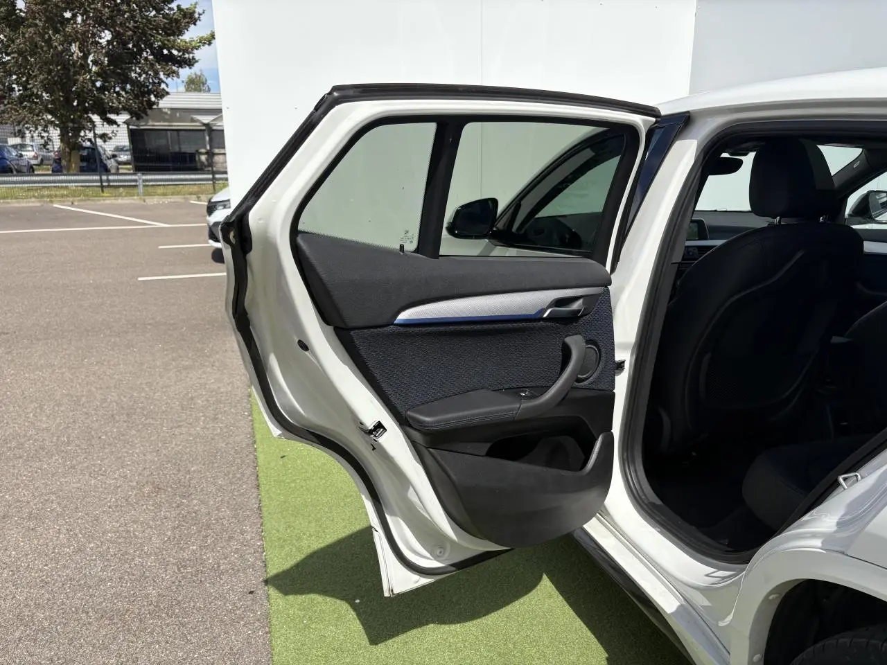 Portière arrière gauche ouverte d'une BMW X2 blanche Alpine, montrant l'intérieur noir avec inserts bleus et poignée intégrée.