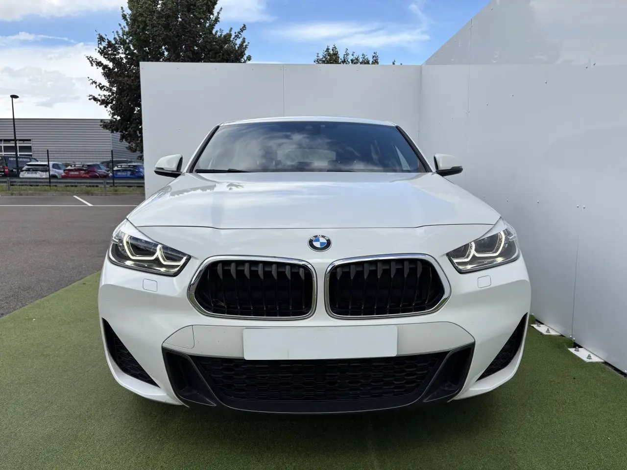 Vue frontale d'une BMW X2 blanche Alpine avec calandre noire et phares LED allumés.