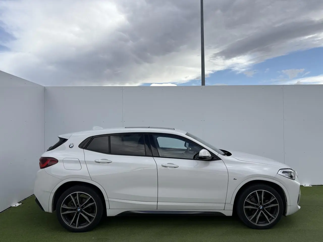 Profil côté gauche d'un BMW X2 blanc alpin avec jantes 19 pouces et toit ouvrant panoramique en verre.