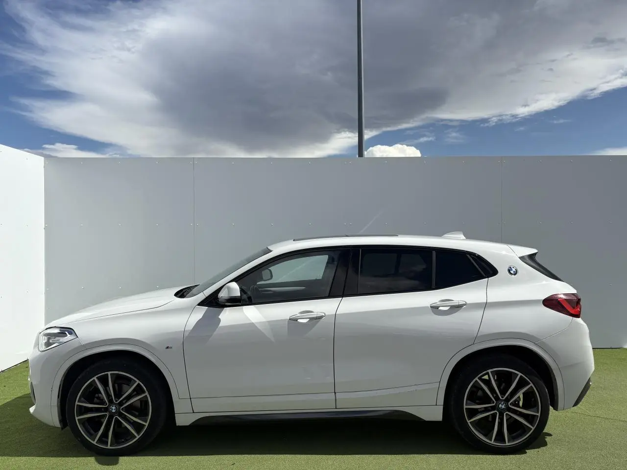 Profil côté gauche d'un BMW X2 blanc alpin avec jantes alliage 19 pouces et toit ouvrant panoramique en verre.