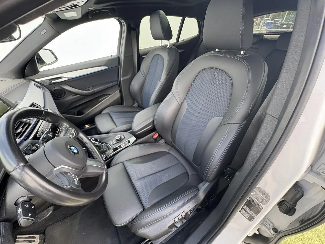 Vue intérieure côté conducteur du BMW X2 blanc avec sièges sport en tissu et similicuir noir et bleu.