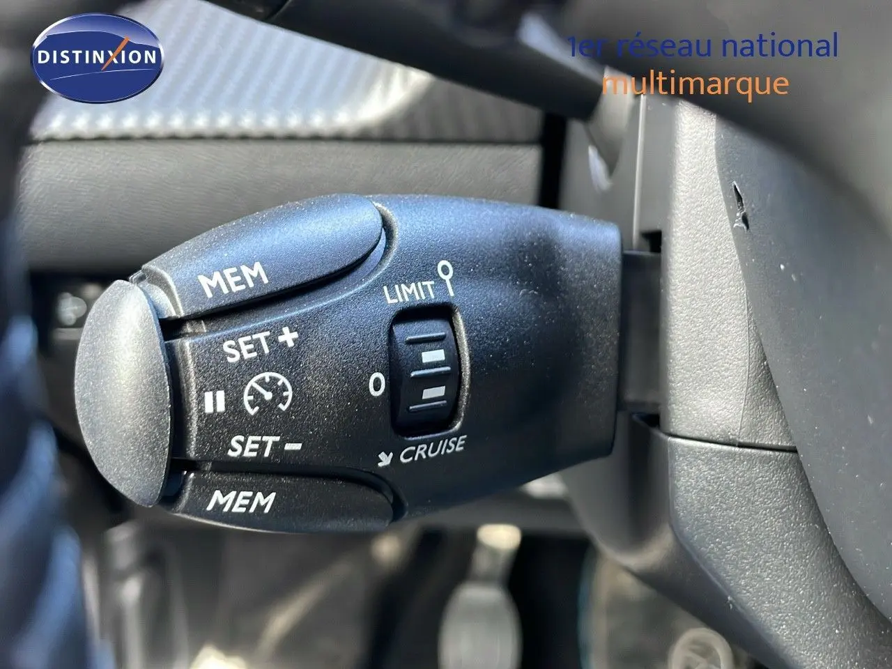 Gros plan sur la commande de régulateur de vitesse à gauche du volant dans l'habitacle du Peugeot 2008 blanc Okenite Metal.