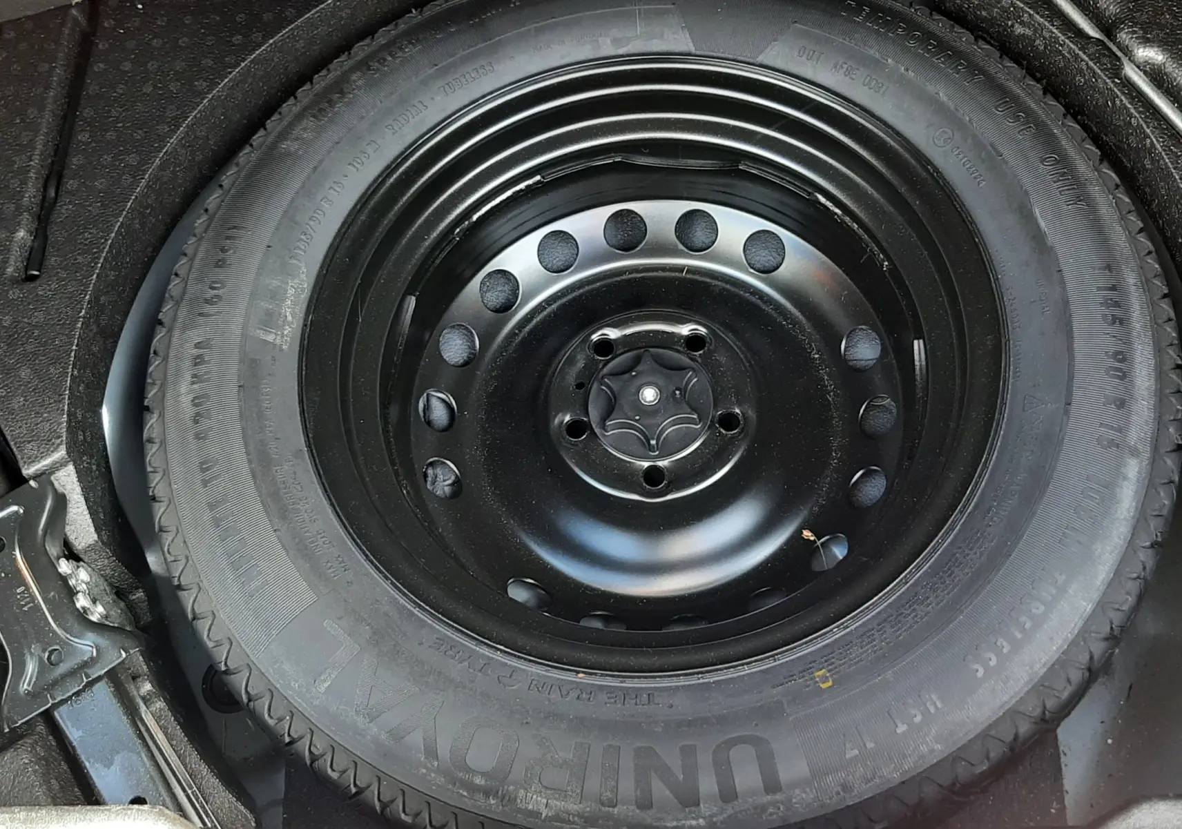 Gros plan sur la roue de secours noire dans le coffre d’un Renault Kadjar gris titanium, vue de dessus.