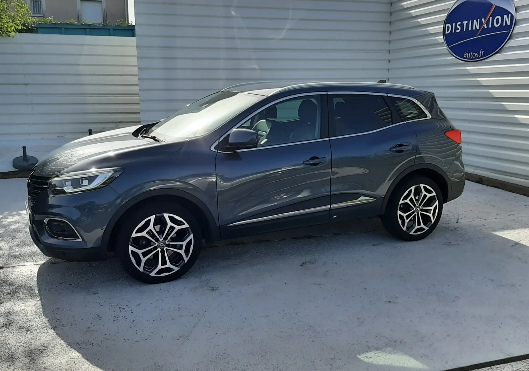 Renault Kadjar gris titanium vu de profil côté gauche, avec jantes alliage et carrosserie lisse sous un ciel clair.