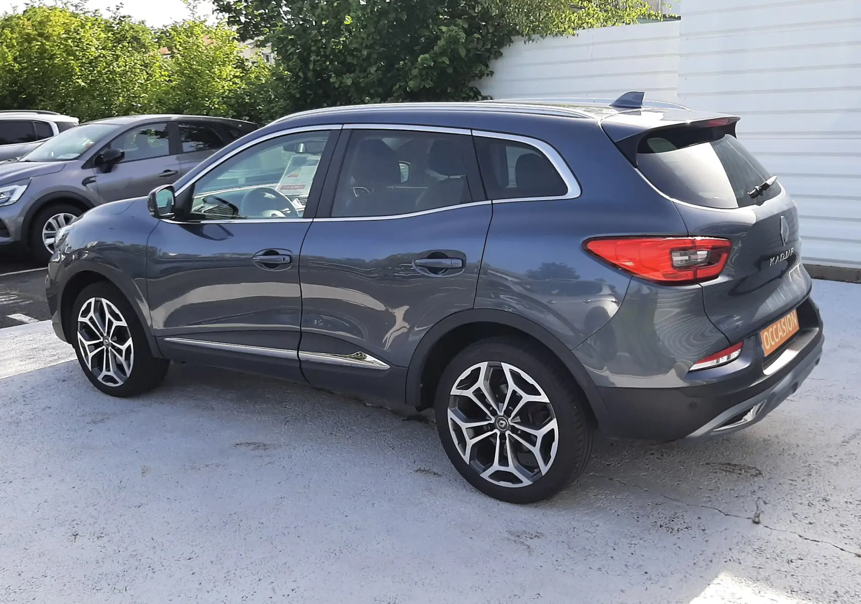 Vue 3/4 arrière droite d'un Renault Kadjar gris titanium 2021 avec jantes alliage et badge "Occasion" à l'arrière.