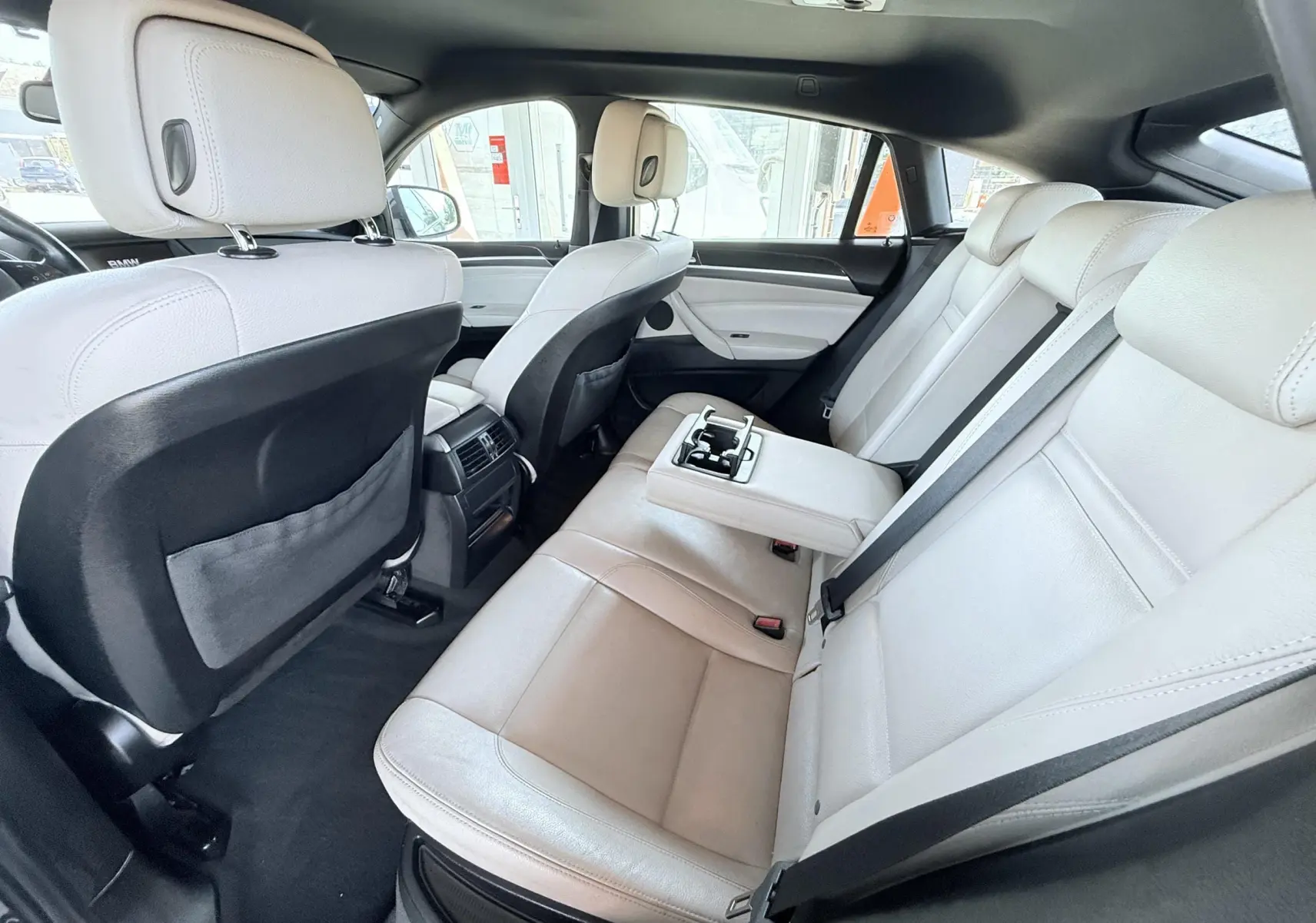 Vue intérieure arrière droite du BMW X6 2011, sièges cuir beige avec accoudoir central déployé et ceintures noires.