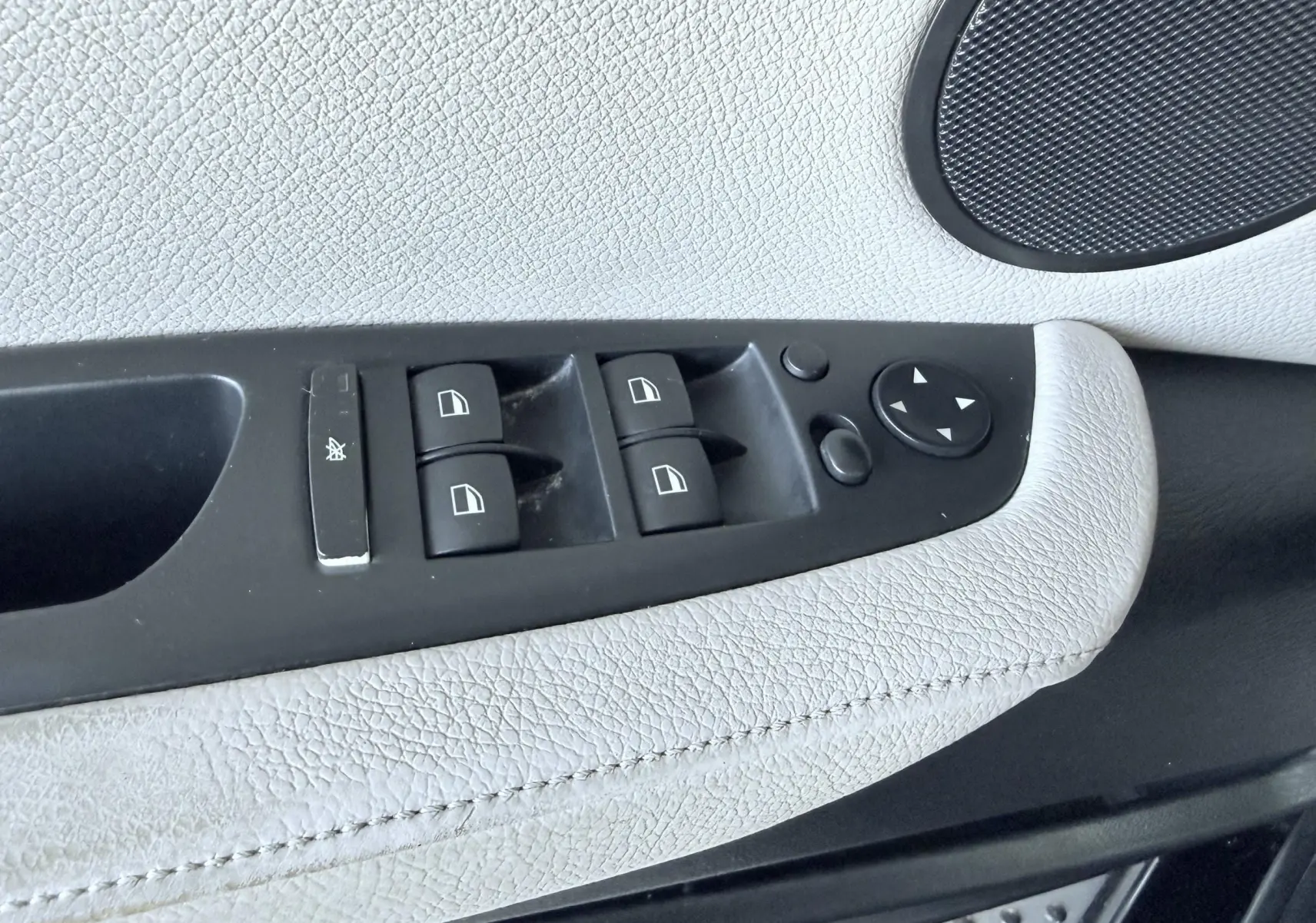 Gros plan sur les commandes des vitres électriques et rétroviseurs sur la portière intérieure en cuir clair du BMW X6 noir.