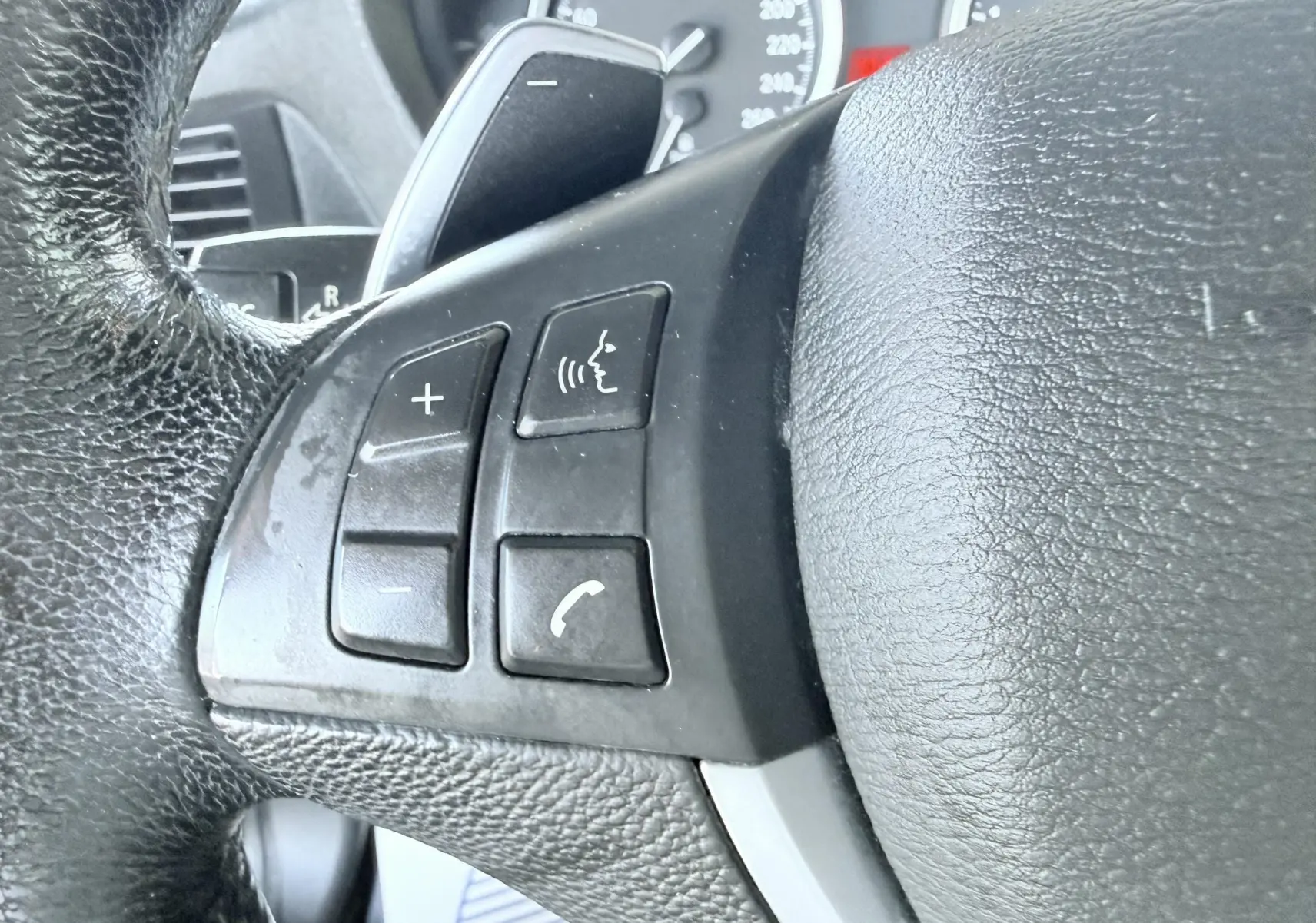 Gros plan sur les commandes vocales et téléphone du volant en cuir noir d’un BMW X6 diesel de 2011.