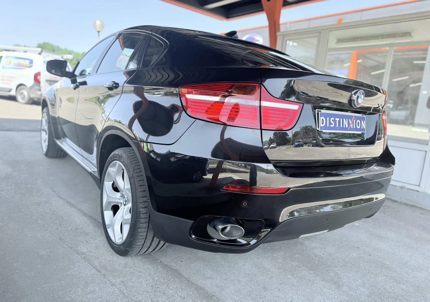 BMW X6 noire vue en 3/4 arrière droit, mettant en valeur ses feux rouges et sa sortie d’échappement chromée.
