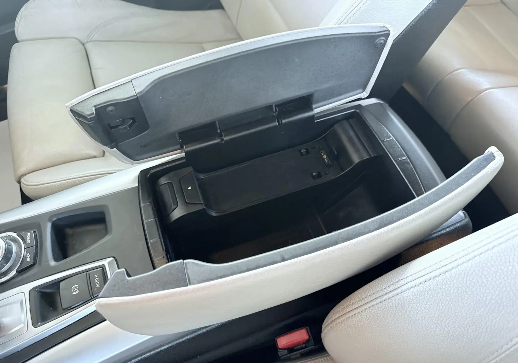 Vue rapprochée de la console centrale ouverte avec rangement, sièges cuir beige clair d’une BMW X6 noire.
