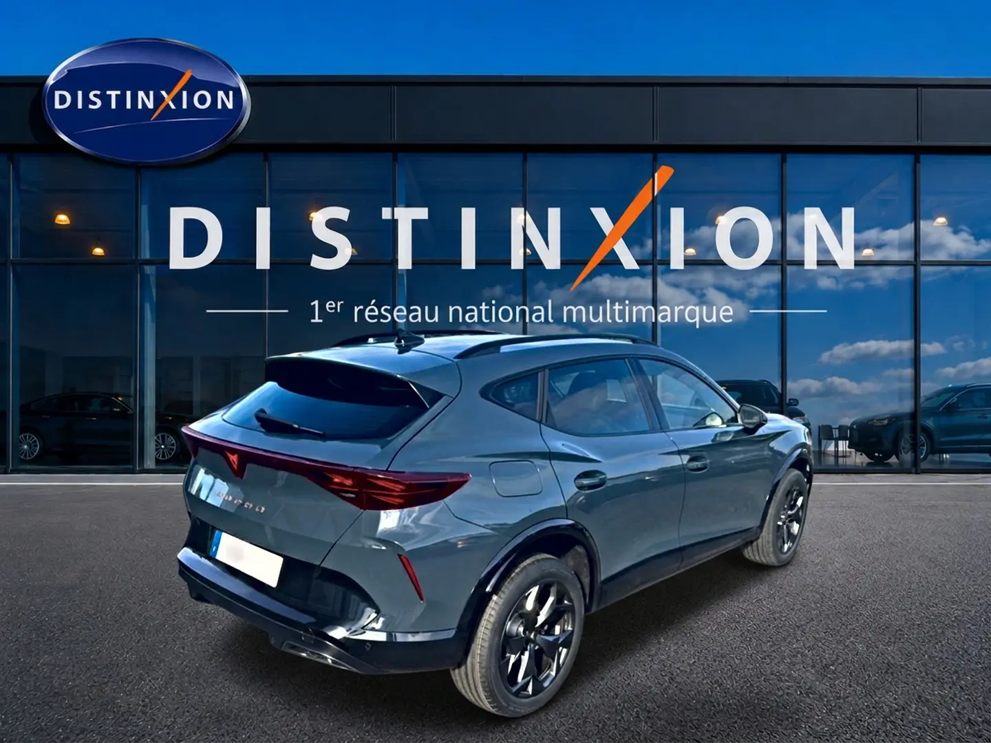 Vue 3/4 arrière droite d'un CUPRA Formentor 1.5 eTSI hybrid bleu fjord avec jantes noires devant une vitrine Distinxion.