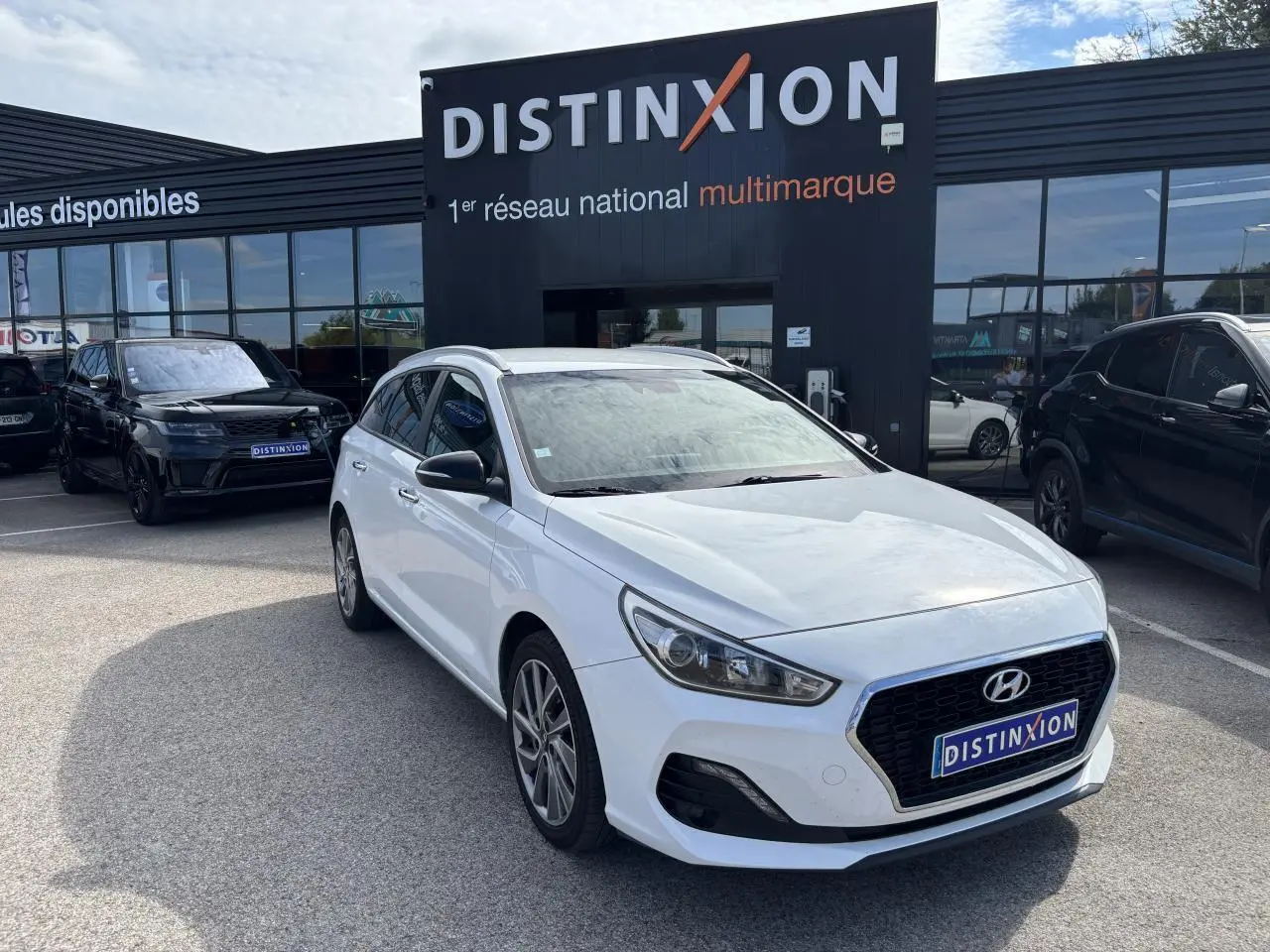Hyundai i30 SW blanche vue 3/4 avant droit devant un showroom Distinxion avec jantes alliage 17 pouces.