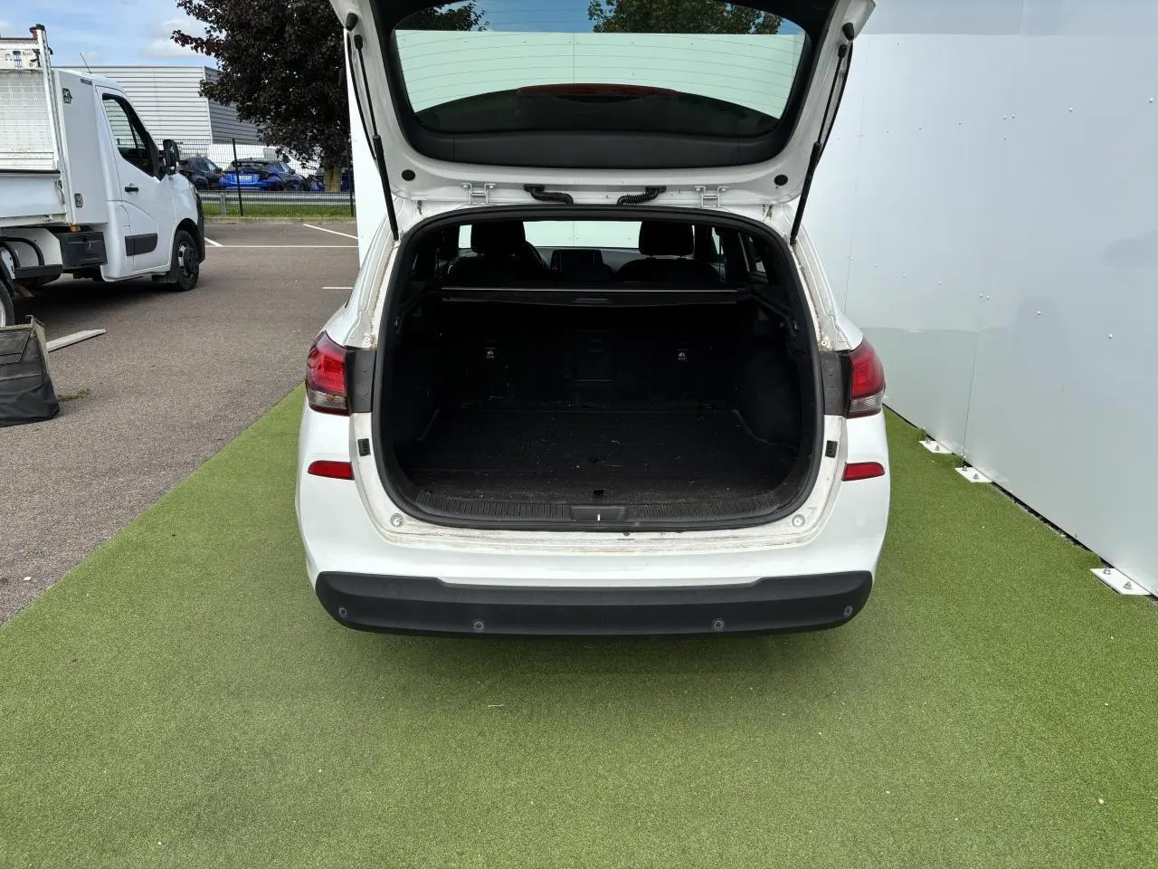 Vue arrière d'un break Hyundai i30 blanc avec coffre ouvert montrant un espace de chargement vide.