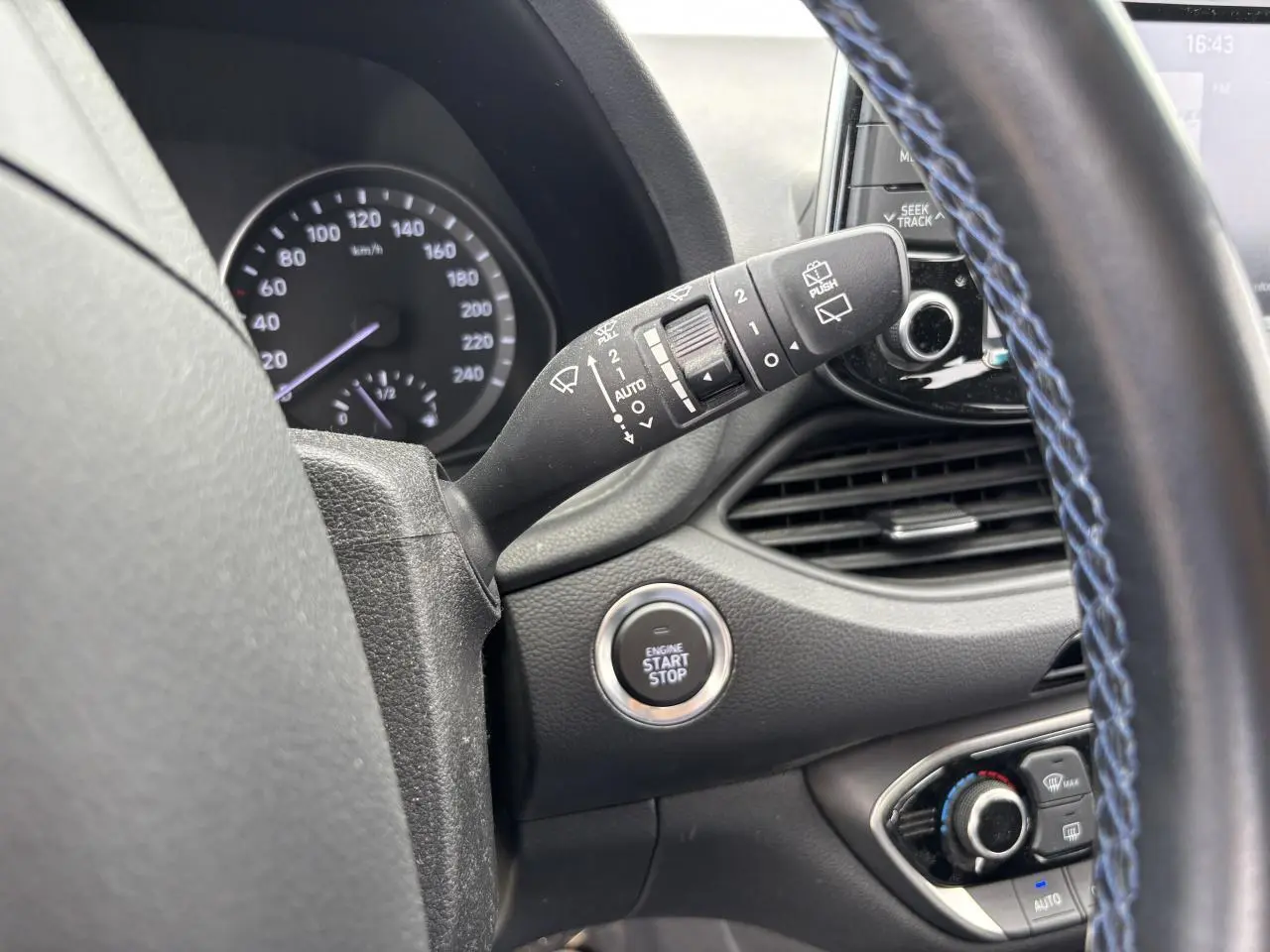 Gros plan intérieur sur le volant avec surpiqûres bleues, bouton start/stop et commandes d'essuie-glace Hyundai i30 SW blanche.