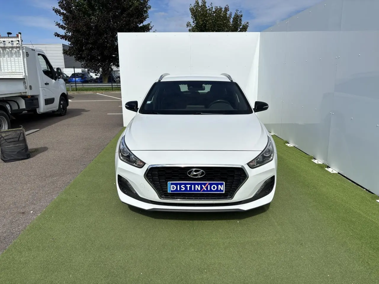 Vue frontale d'une Hyundai i30 SW blanche avec calandre noire et plaques Distinxion sur un sol vert.