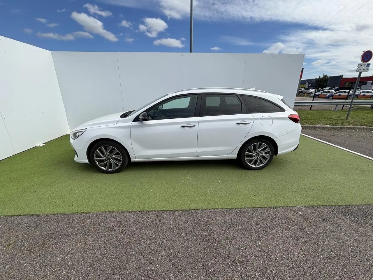 Vue latérale côté gauche d'une Hyundai i30 SW blanche garée sur sol vert avec jantes alliage et vitres surteintées.