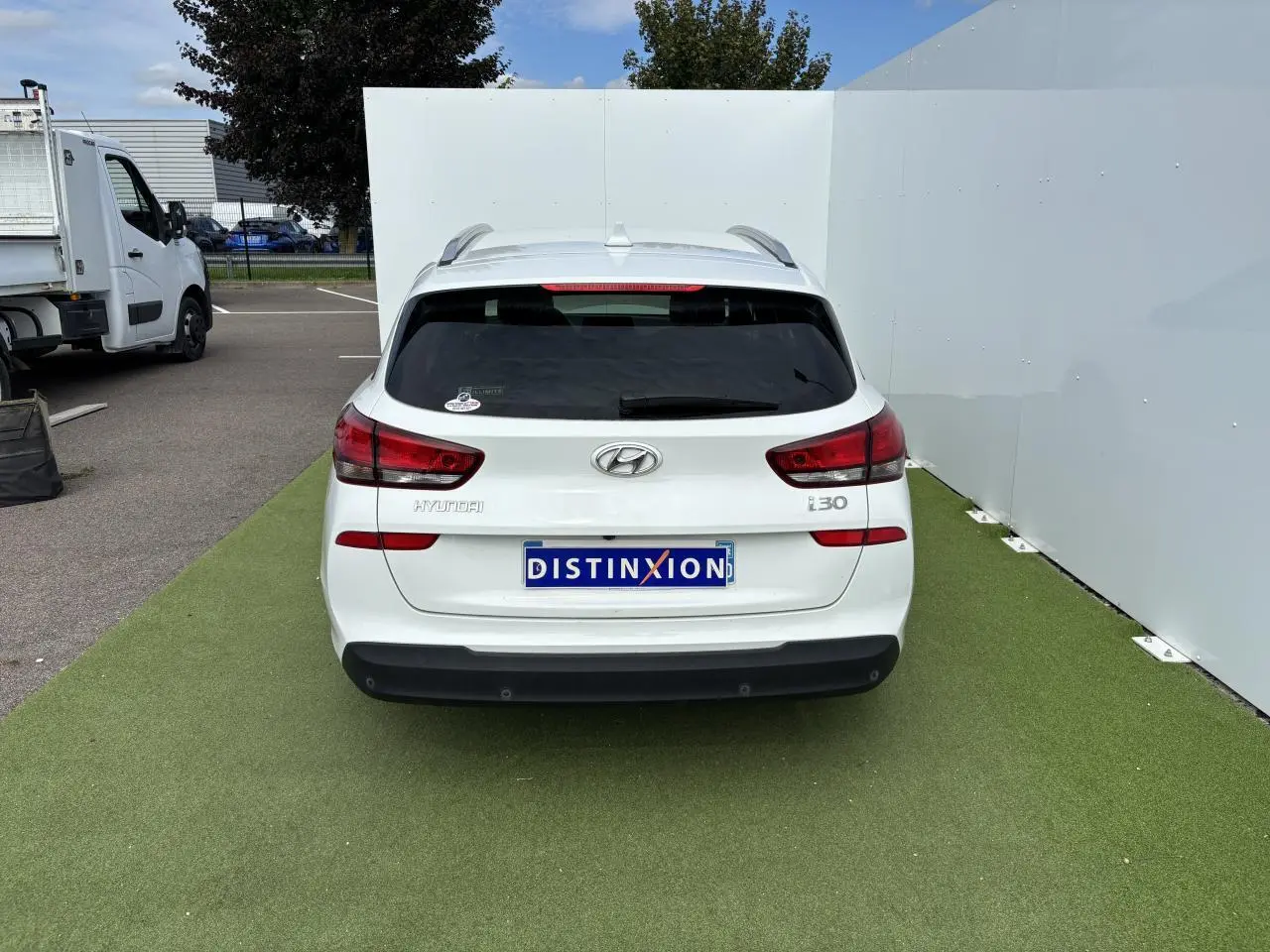 Vue arrière d'une Hyundai i30 blanche stationnée sur sol vert avec logo et feux arrière visibles.
