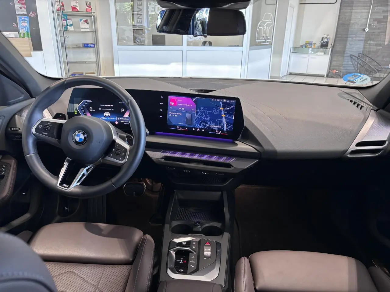 Vue intérieure de la BMW Série 1 120d M Sport 2025, tableau de bord moderne avec écran tactile et éclairage d'ambiance violet.