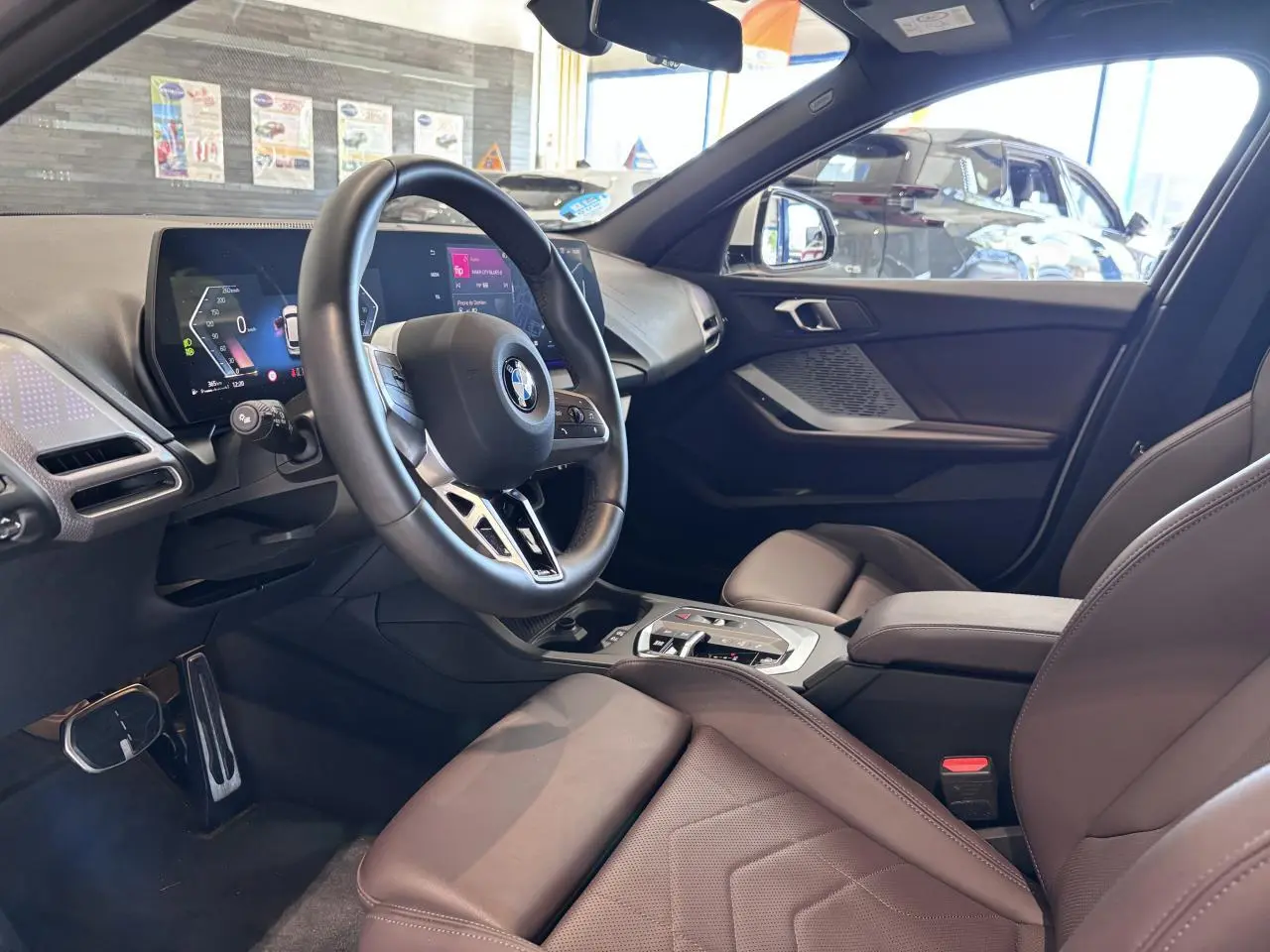 Vue intérieure côté conducteur de la BMW Série 1 120d M Sport 2025 avec volant multifonction et sellerie cuir marron.