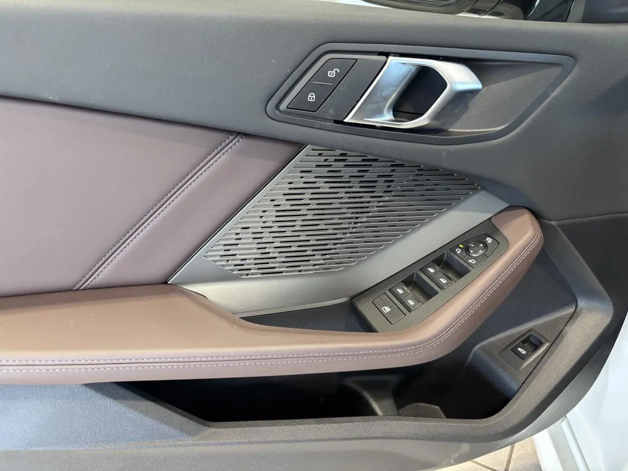 Détail de la porte côté gauche d’une BMW Série 1 120d M Sport 2025, avec garniture marron et commandes de vitres.