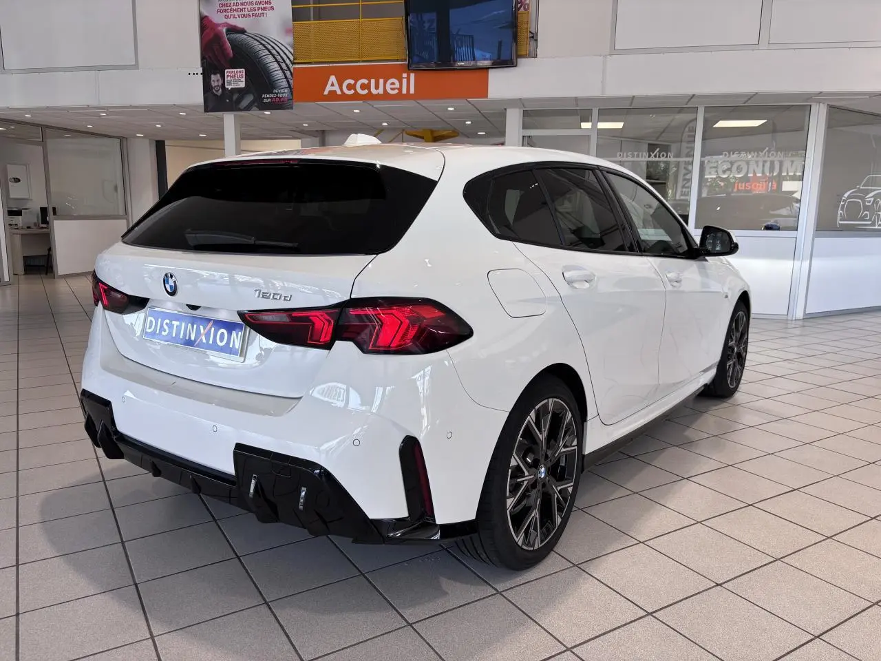 Vue 3/4 arrière droite d'une BMW Série 1 120d M Sport blanche, avec jantes sport et diffuseur noir, en showroom.