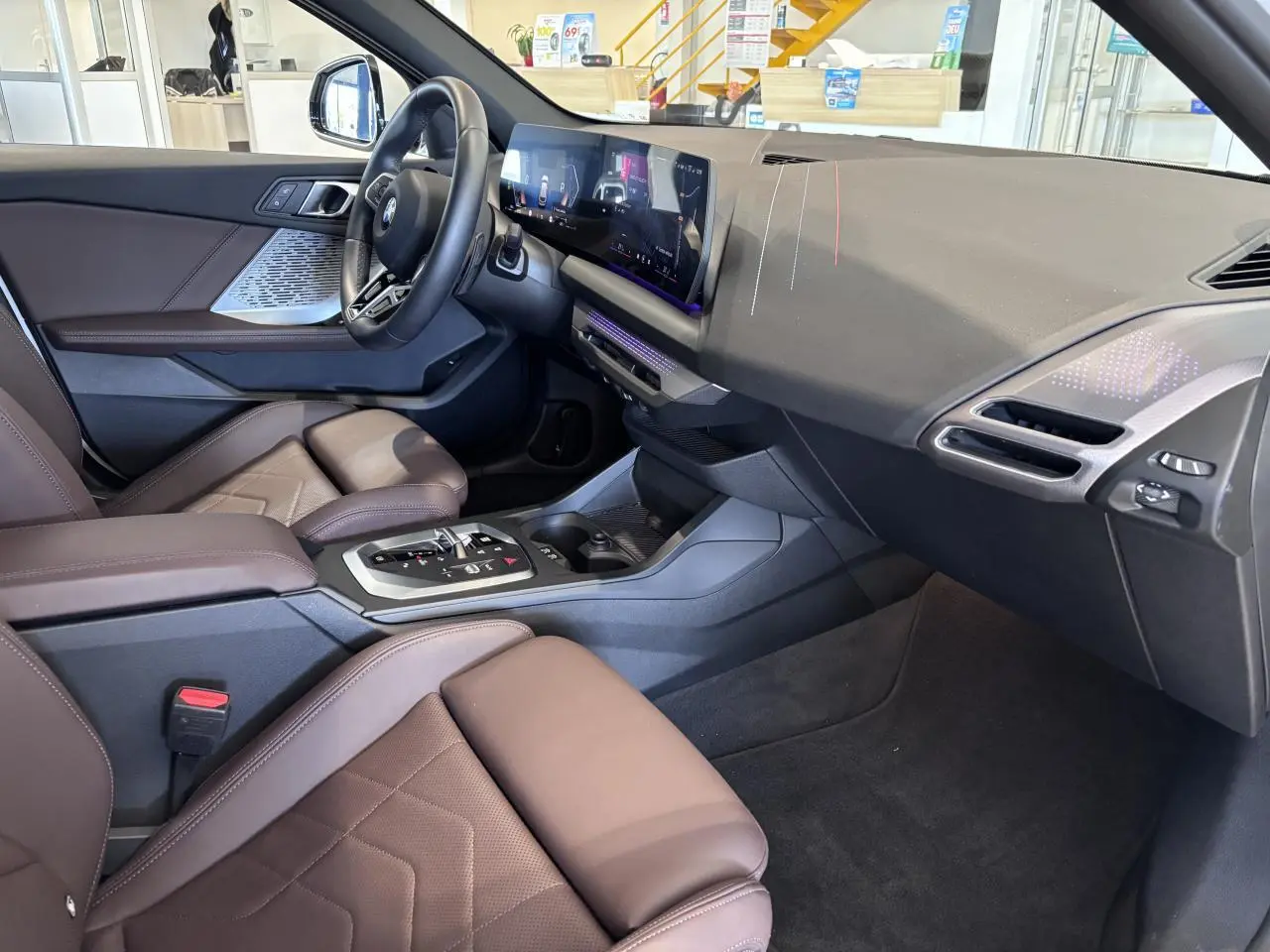 Vue intérieure côté conducteur de la BMW Série 1 120d M Sport 2025 avec sellerie cuir marron et tableau de bord moderne.