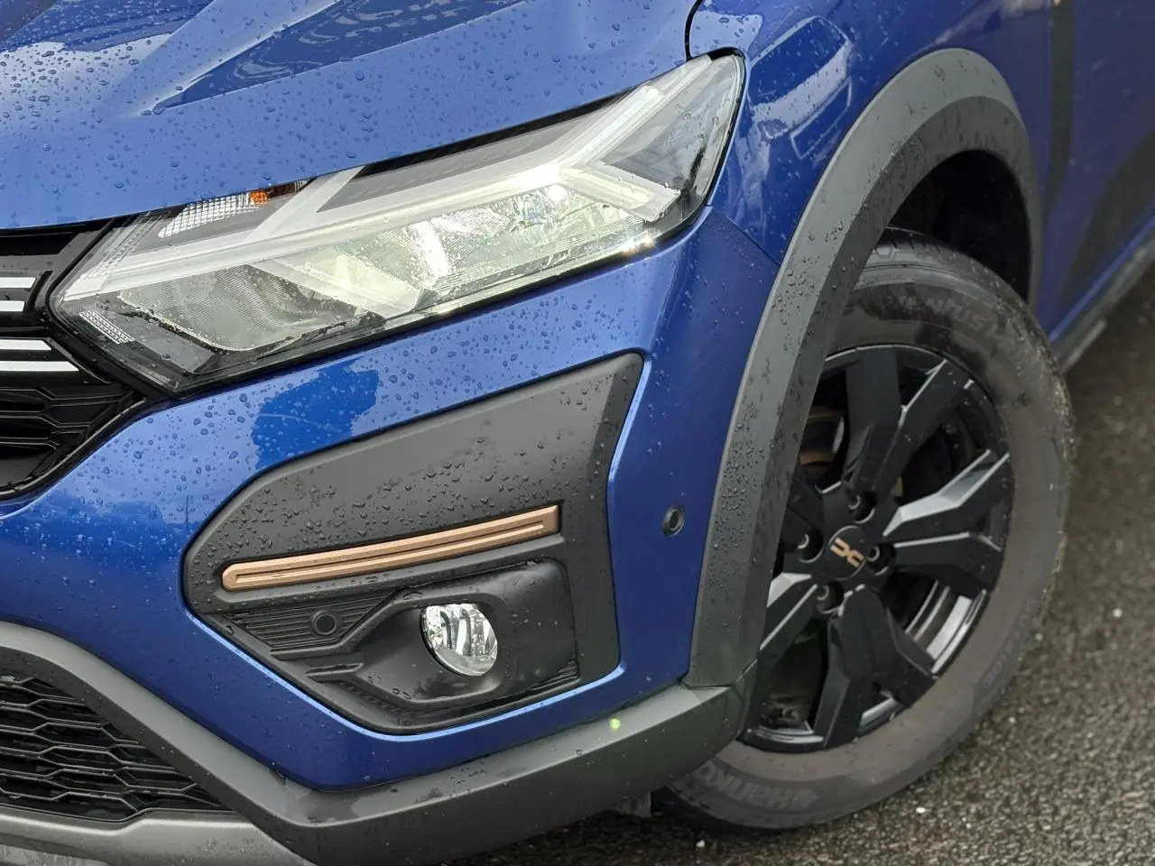 Gros plan sur l'avant droit bleu Iron du Dacia Sandero Stepway 2025, avec phare LED et jante alu noire distinctive.