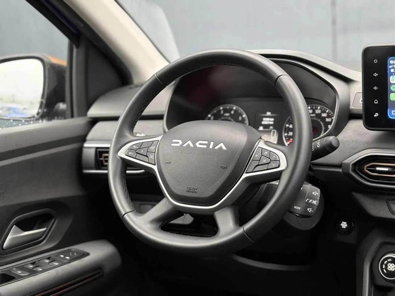 Vue intérieure centrée sur le volant noir Dacia avec commandes intégrées et écran tactile à droite.
