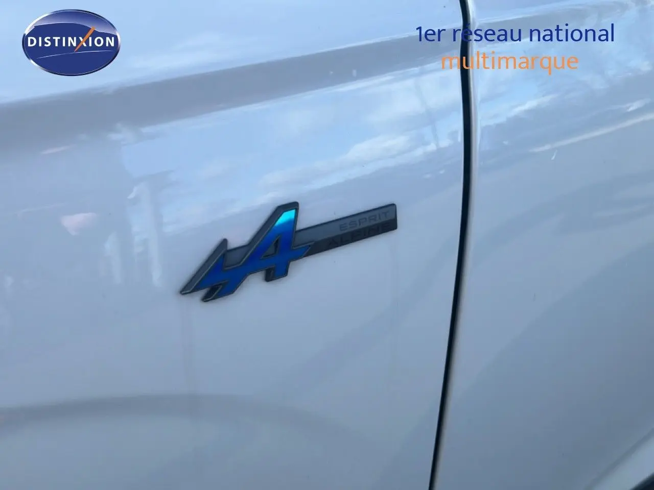 Gros plan sur l'écusson Esprit Alpine bleu sur la portière blanche du Renault Austral Iconic 2024 hybride.